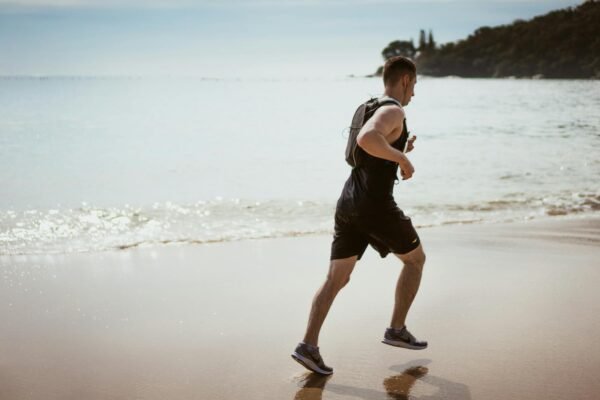 Man Wearing Black Tank Top and Running on Seashore